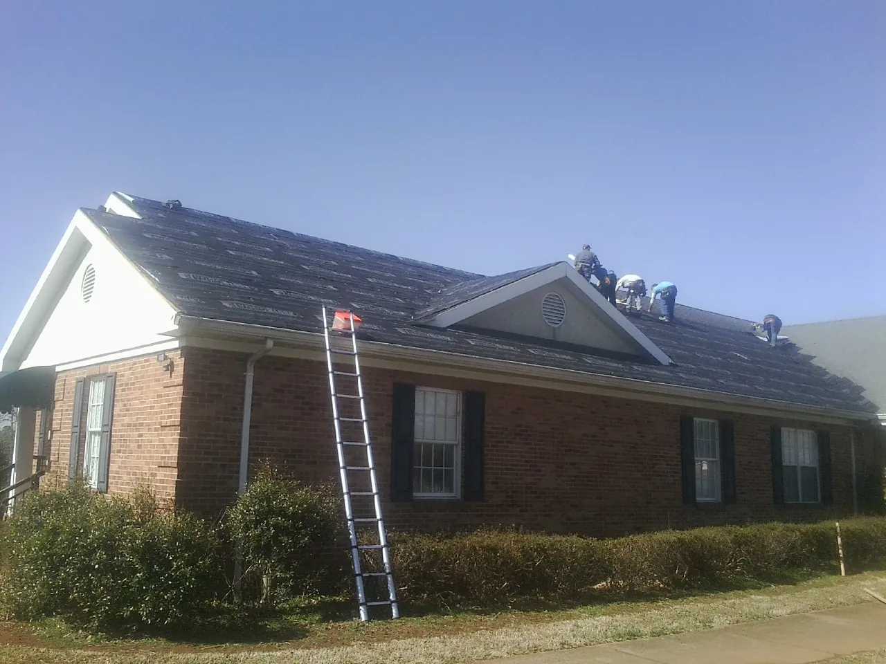 Crew tearing shingles off a brick ranch roof with a ladder set — Emergency Roof Repair work by our crew in Ithaca
