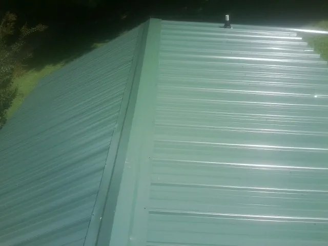 New green metal panels meeting at the ridge of a roof — Flat Roof Repair work by our crew in Ithaca