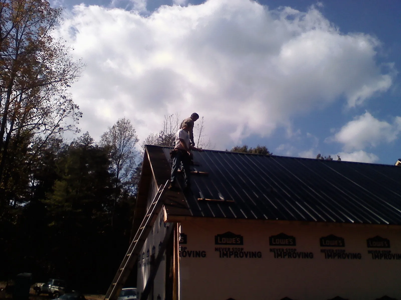 Roofer fastening dark metal panels high against a cloudy sky, from a Roof Inspection job in Ithaca