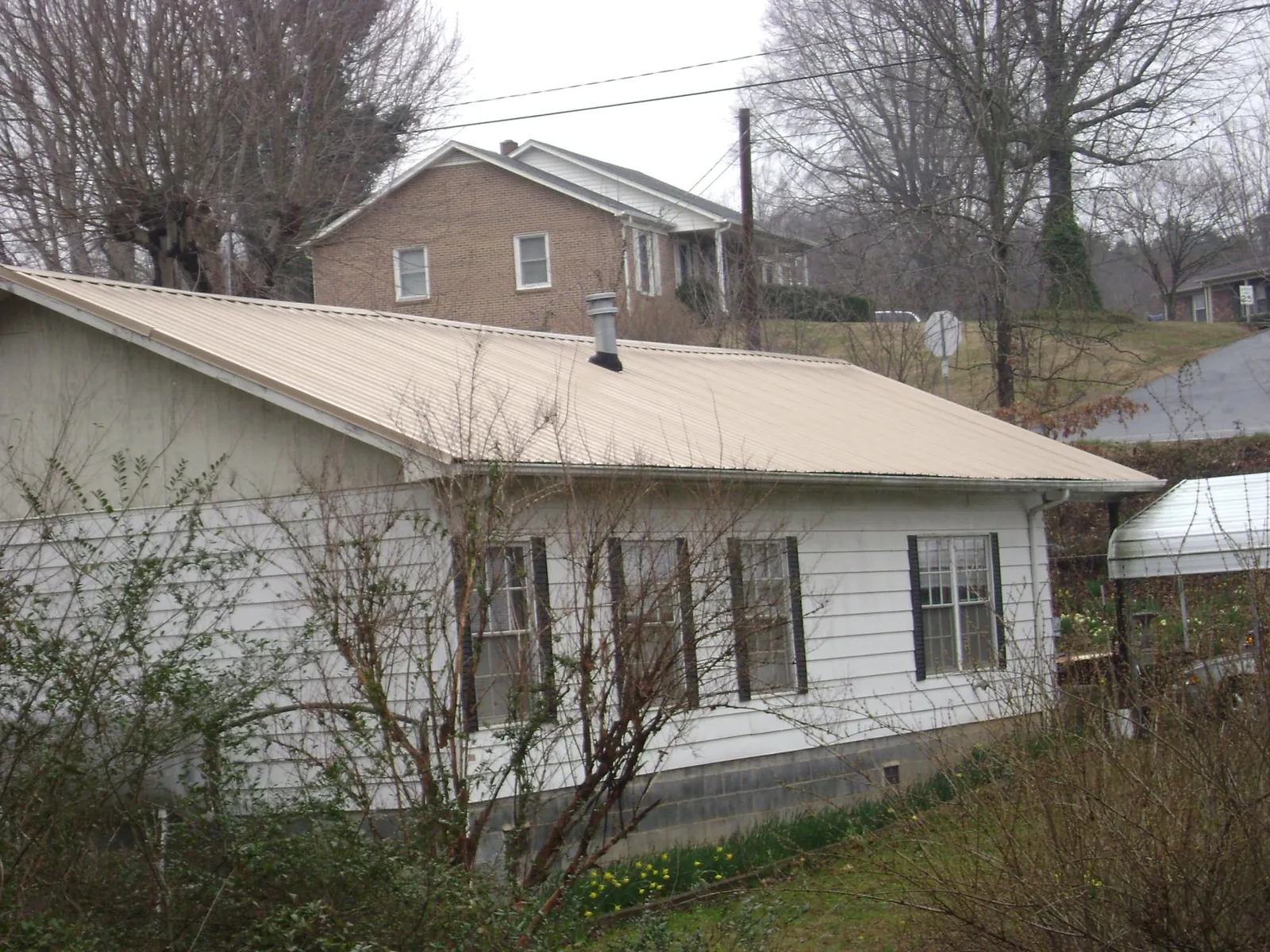 Tan metal roof on a white sided house set into a hillside — Commercial Roofing by Roofing Brothers in Ithaca