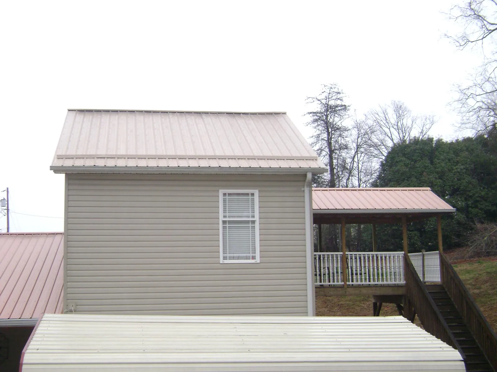 Tan metal roofs on a two story addition and attached porch, from a Roof Replacement job in Ithaca