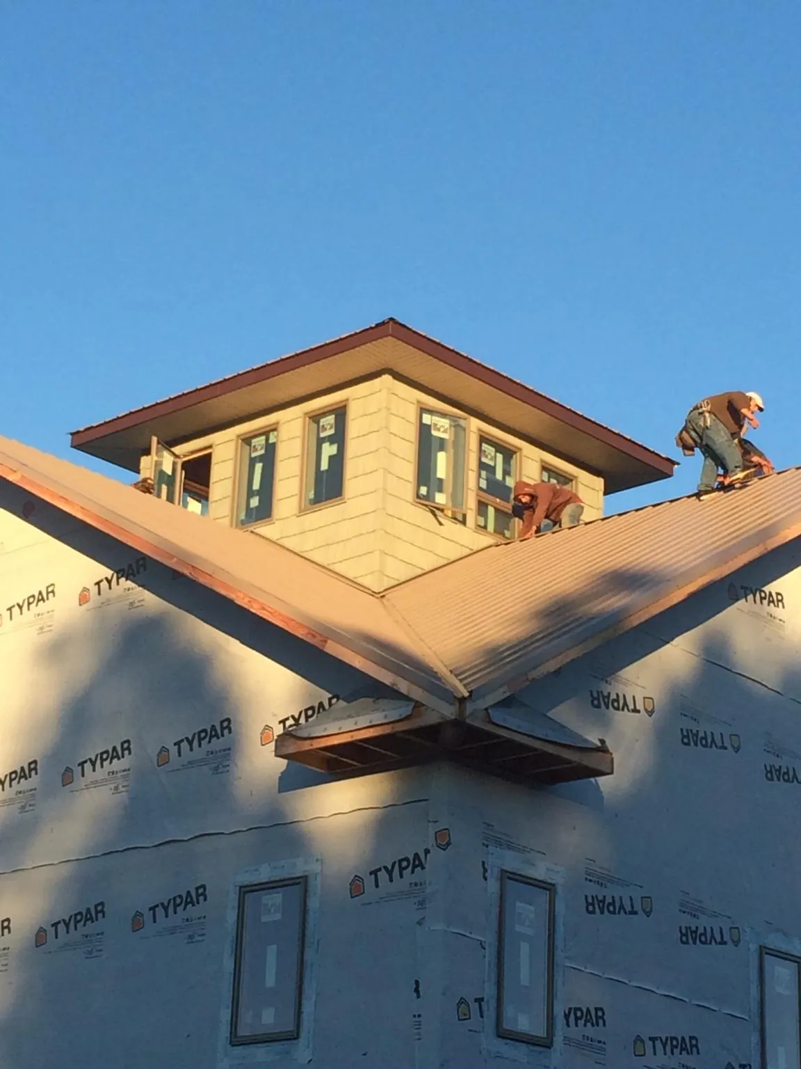 Roofers working around a rooftop cupola on a new metal roof at sunset — Roof Waterproofing in Ithaca by Roofing Brothers